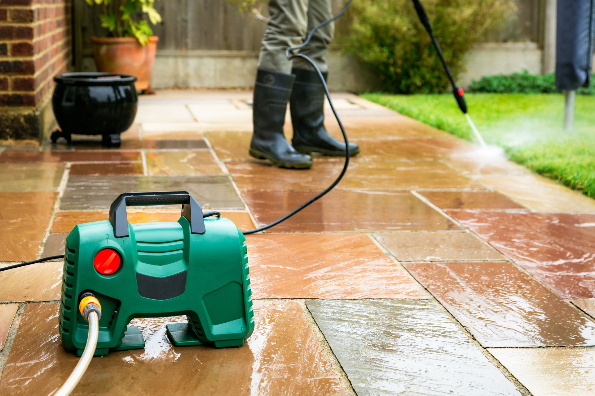 Senior man cleaning patio tiles using pressure washer